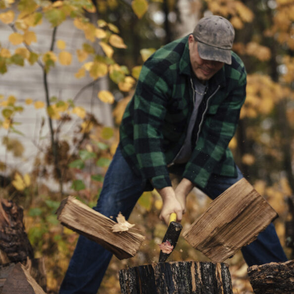 Mature man splitting logs in autumn forest, Upstate New York, USA